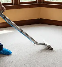Steam carpet cleaning technician using a hot-water extraction wand on a residential carpet, wearing blue protective shoe covers Louisville, KY.