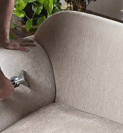 Professional upholstery cleaner deep-cleaning a fabric sofa with a handheld extraction tool and hose Louisville, KY.